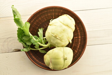 One whole and one half organic kohlrabi cabbage in a clay plate on a wooden table, close-up, top view.