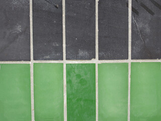 Wall lined with vintage tiles of green and gray color close-up