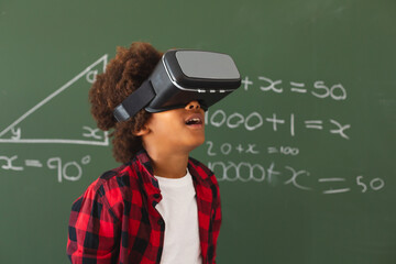 African american schoolboy in front of chalkboard in classroom using vr headset