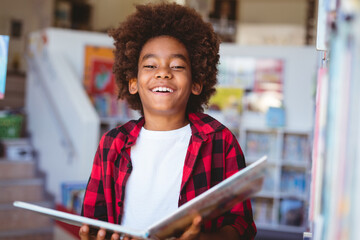 Laughing african american schoolboy reading book standing in school library