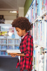 Happy african american schoolboy reading book standing in school library