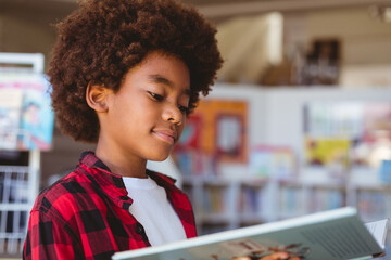Smiling african american schoolboy reading book standing in school library