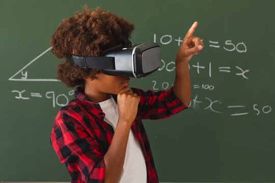 African american schoolboy in front of chalkboard in classroom using vr headset