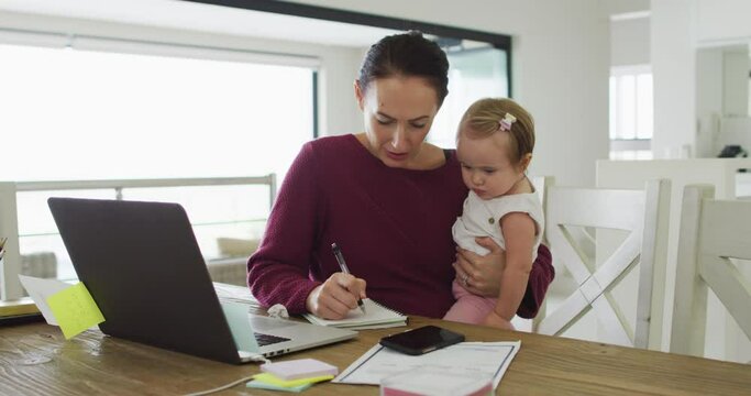 Caucasian mother holding her baby taking notes while working from home