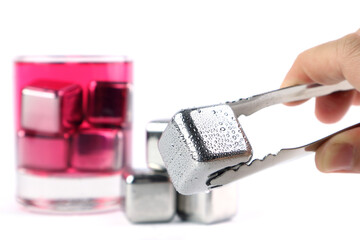 a stainless steel ice cube is picked by ice tong with background of stainless ice cubes and a glass...