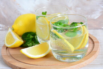 glasses with mineral water, lemon slices, mint leaves on the cutting board on the beige background