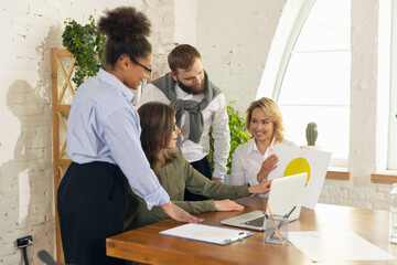 Young man and women, colleagues working together in modern office using devices and gadgets during negotiations