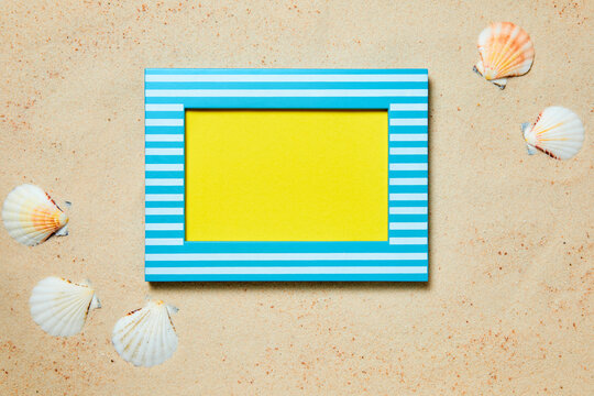 Picture frame with copy space and sea shells on sand as a summer background