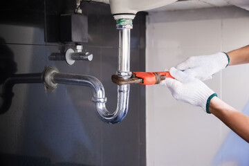 Plumber fixing white sink pipe with adjustable wrench.