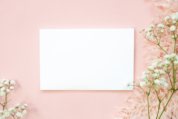 Fototapeta premium Blank white sheet on beige background and natural pink flower. Top view, space for text.
