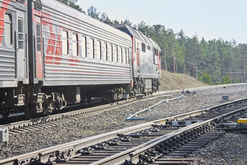 Fototapeta premium The soft focus of a red-gray train and railway against a background of green forest and blue sky. The train travels along the railway tracks through the forest during the day.