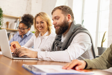 Young man and women, colleagues working together in modern office using devices and gadgets during negotiations