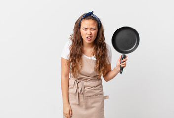 young pretty woman feeling puzzled and confused chef concept and holding a pan
