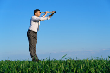 businessman poses with a spyglass in a green field, he looks an idea or something, business concept, green grass and blue sky as background