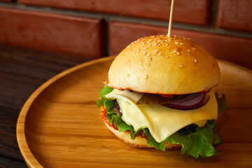 Burger with beef, cheese and lettuce leaves on a wooden plate on a brick wall background. Close-up, selective focus