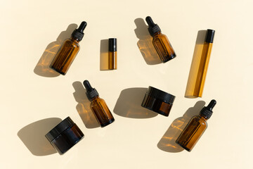 Bottles of dark amber glass with essential oil and face cream on a beige background. Natural SPA...