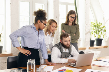 Young man and women, colleagues working together in modern office using devices and gadgets during negotiations
