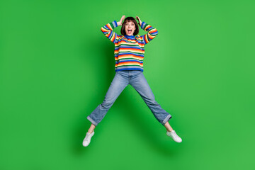 Fototapeta na wymiar Full length photo adorable impressed lady dressed colorful pullover jumping high arms head smiling isolated green color background