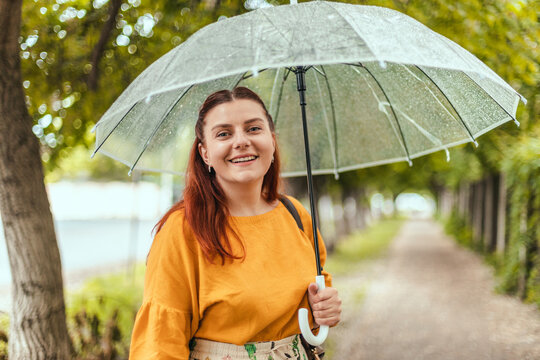 Happy young woman with transparent umbrella under rain outdoors