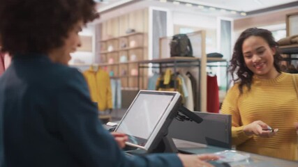 Clothing Store Checkout Cashier Counter: Woman and Male Retail Sales Managers Accept NFC Smartphone and Credit Card Payments from a Young Female Customers for Clothes and Pack Them in Recyclable Bags. - Powered by Adobe