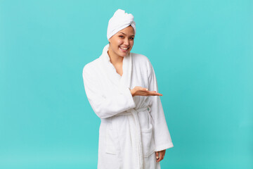 young pretty woman smiling cheerfully, feeling happy and showing a concept and wearing bath robe...