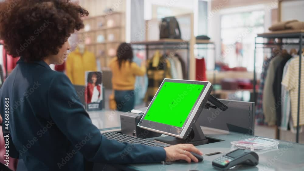 Wall mural Clothing Store Checkout Cashier Counter: Stylish Female Retail Sales Manager with Afro Hair Working at a Cash Point with Money Register Computer with Green Screen Chroma Key Mock Up Display.