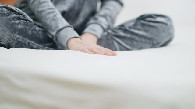 Young slim female Caucasian hand stroking white clean linen on bed. Unrecognizable happy woman admiring fresh bedsheet in bedroom in the morning. Cleanliness and coziness concept