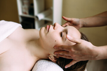 Masseur doing massage on a woman's face at the spa.