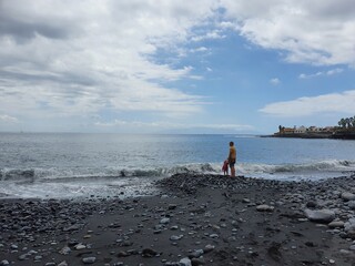 Father and daughter, standing on the sea shore, watching the waves on a cloudy day