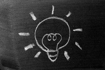 White chalk hand drawing in light bulb shape on blackboard or chalkboard background (Concept for new idea or creativity)