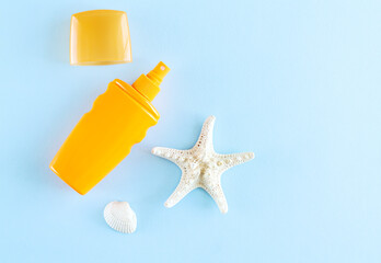 Summer sunscreen or spray next to sea shell and starfish on blue background