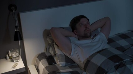 Lonely man cannot sleep in bed at night with eyes wide open, staring at ceiling. Male lying in bed, stressed, worried and cant sleep. Insomnia. Sleepless guy addicted to smartphone instead of sleep