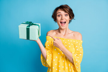 Photo of festive happy astonished young woman point finger present box holiday isolated on blue...