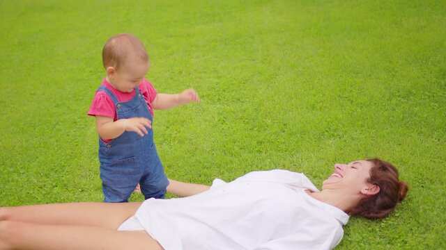 Baby girl with mother on the grass in the summer sunlight in park. Happy family concept. Child with mother happy.