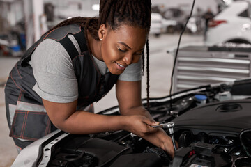 Smiling Caucasian Female Mechanic is Working With Car In Car Service. Woman in Overalls is Working...