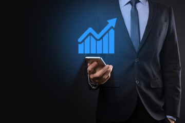 Businessman holding tablet and showing a growing virtual hologram of statistics, graph and chart with arrow up on dark background. Stock market. Business growth, planing and strategy concept.