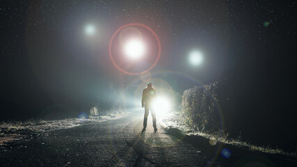 Naklejka premium UFO concept. Glowing orbs, floating above a misty road at night. With a silhouetted figure looking at the lights.