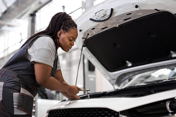 Black Female car mechanic holding wrench checking up on the car engine, for repair and checkup,...