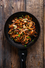 Roasted mushrooms with onion in frying pan on a wooden background. Top view