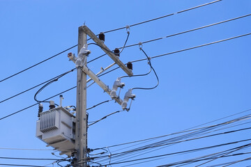 Drop fuse and transformer on cement high voltage pole with blue sky close-up.