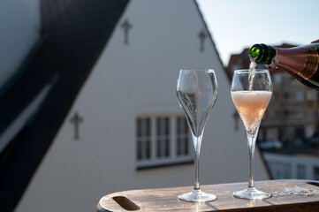 Pouring of rose champagne sparkling wine in flute glasses on outdoor terrace in France