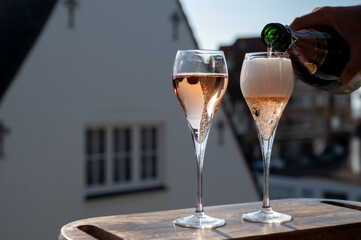 Pouring of rose champagne sparkling wine in flute glasses on outdoor terrace in France