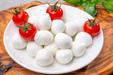Italian tricolore, small balls of fresh white soft Italian mozzarella cheese, ripe red cherry tomatoes and fresh green basil herb, ready for making caprese salad