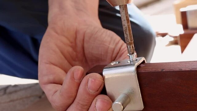 A man assembles wooden furniture and uses a tool to screw the screws into a wood product. Repair and diy. The worker connects the parts of the structure and fixes the parts.
