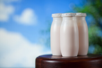 Natural liquid yogurt with probiotics in small plastic bottles on wooden table on background of blue sky with clouds. Healthy, balanced diet food, healthy breakfast, dairy products.