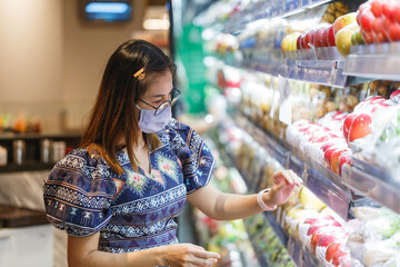 Asian woman wearing protect face mask and  shopping fruit, vegetable in grocery department store.