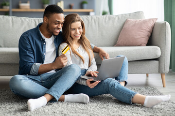 Online Shopping. Cheerful Mixed Couple Using Laptop And Credit Card At Home