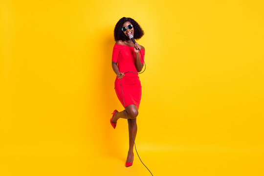 Full size photo of young beautiful gorgeous happy afro girl in sunglasses singing karaoke isolated on yellow color background