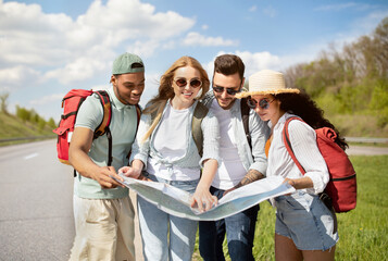 Group of best friends with backpacks checking map during road trip, hitchhiking on highway