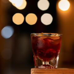 Glass of expensive alcoholic drink with ice cube. Cold strong beverage on black background with backlit bokeh. Copy space for text.